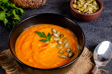 Vegetarian autumn cream soup of pumpkins and carrots with seeds and parsley on a dark background