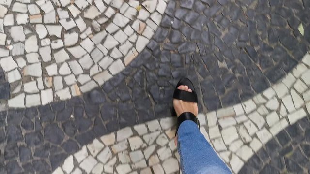 POV. Feet in black sandals, classic blue jeans, walk on the sidewalk.