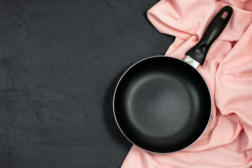 Empty black frying pan with pink kitchen towel on black table.