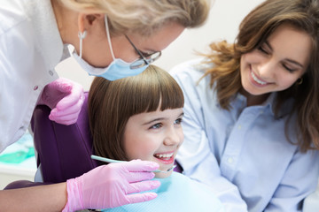 Fototapeta premium Doctor examining child teeth with instrument and mirror. Mother controlling process. 