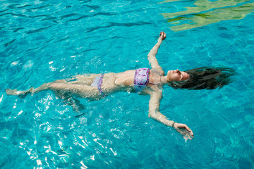 Beautiful young woman floating in pool on his back in hot summer day