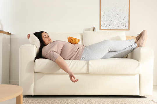 Lazy overweight woman with chips resting on sofa at home