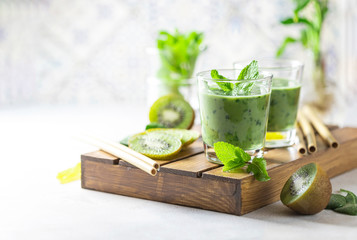 Detox green smoothie - kiwi, spinach and matcha on a light grey slate, stone or concrete background.