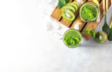 Detox green smoothie - kiwi, spinach and matcha on a light grey slate, stone or concrete background.