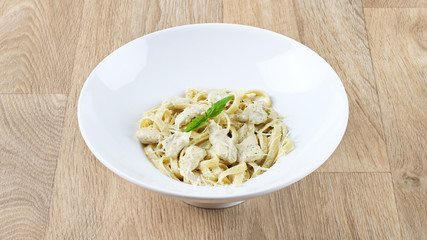 alfredo pasta with basil leaves and Parmesan cheese in a white plate on a wooden background