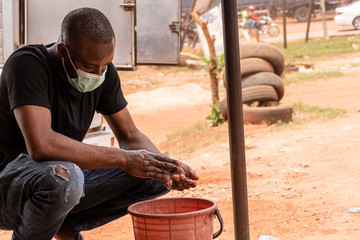 african man wearing face mask washing his hands outdoor with soap and water
