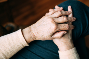Two old woman's hands resting on her leg