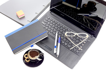 Laptop, glasses, pen, notebook and cup of coffee on a table close-up.