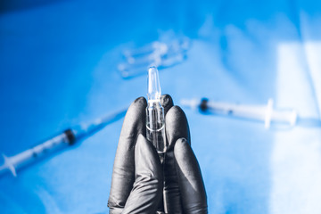 Hands in black gloves with hepatitis vaccine in a transparent bottle. Immunization and treatment of...