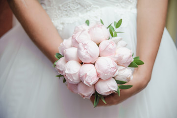 Delicate bouquet of pink flowers in the hands of the bride. Unusual wedding stylish bouquet with pink peonies. Wedding dress, details