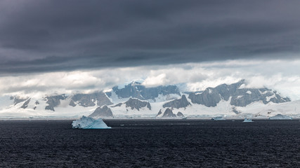 glacier in the mountains coastline of antarctica with rocks and snow at the sea with clouds and iceberg 
