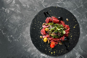 Beef carpaccio with arugula on a black plate, traditional Italian cuisine. Dark key, copy space,