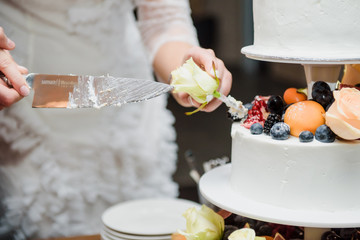 A bride and a groom is cutting their fruit wedding cake on wedding banquet. Hands cut the cake with...