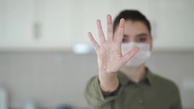 Portrait of a young woman in protective mask showing stop gesture in light room. health and safety life concept, proliferation prevention covid 19 coronavirus.