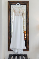 Elegant wedding white dress hanging on a wooden door during a wedding preparation. Bride's morning. Before ceremony