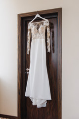 Elegant wedding white dress hanging on a wooden door during a wedding preparation. Bride's morning. Before ceremony