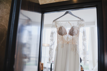 Elegant wedding white dress hanging on a wooden door during a wedding preparation. Bride's morning. Before ceremony