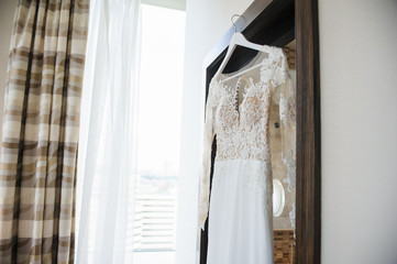 Elegant wedding white dress hanging on a wooden door during a wedding preparation. Bride's morning. Before ceremony