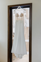 Elegant wedding white dress hanging on a wooden door during a wedding preparation. Bride's morning. Before ceremony