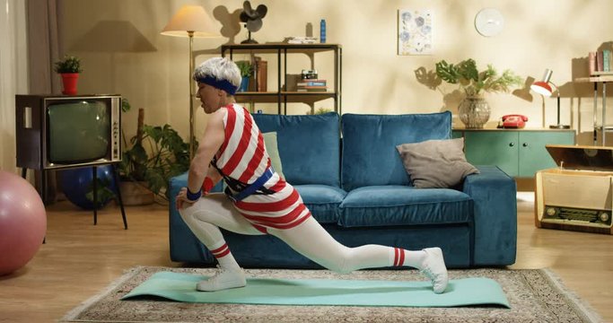 Side view of funny old grey-haired woman having work out on yoga mat in room at home. Pretty Caucasian senior female retro style model stretching muscles indoors. Sport concept
