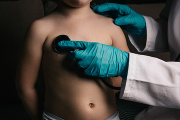 Close up of medical doctor hands with protective gloves, using stethoscope to perform pulmonary examination on a toddler.