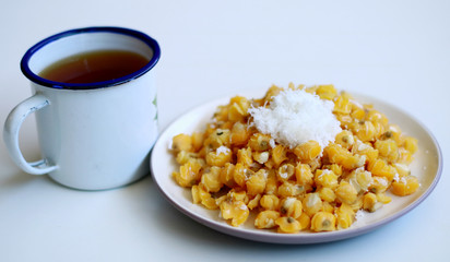 Grontol jagung and a cup of tea on white background.  Grontol jagung is traditional snacks in Indonesia. Boiled shelled corn sprinkled with grated coconut.