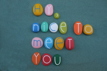 Hy, nice to meet you, creative text composed with multi colored stone letters over green sand