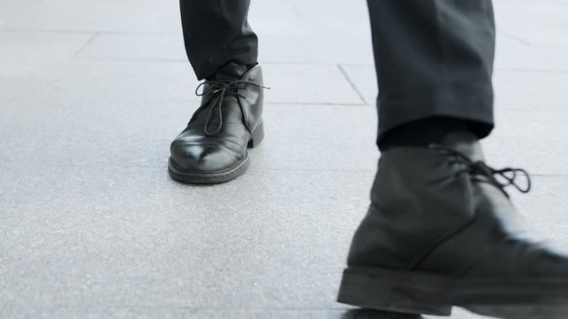 Businessman in black shoes going for job. Man legs walking on city road