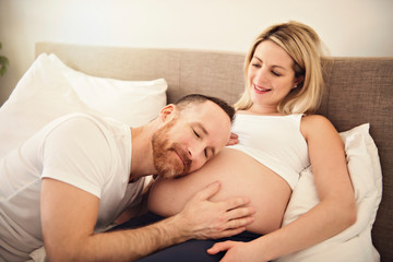 Obraz na płótnie Canvas Beautiful pregnant woman and her handsome husband spending time together in bed ear belly