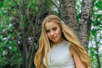 Portrait of a charming blond woman wearing beautiful white dress standing next to rowan tree.