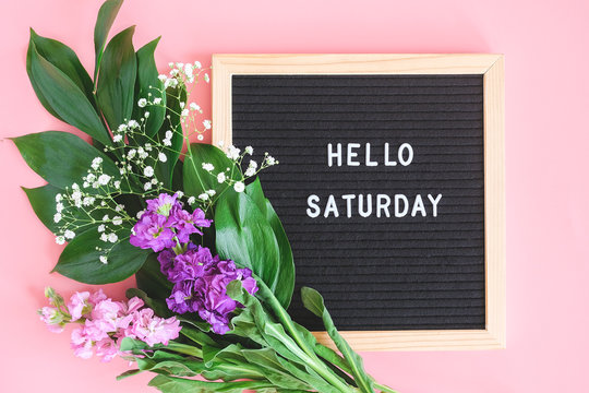 Hello Saturday text on black letter board and bouquet colorful flowers on pink background. Concept Happy Saturday. Template for postcard, greeting card Flat lay Top view