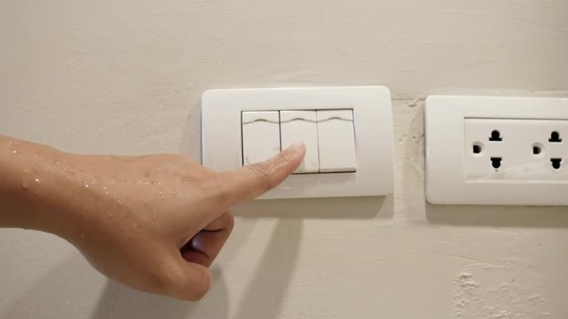 Close-up wet of female hand or fingers turn off on white light switch on white wall in the night time at home. Saving Electrical. Concept of do not use electricity with wet hand and safety.
