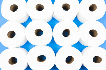 Background pattern of toilet paper rolls lay flat on the bright blue background. Coronavirus pandemic panic shopping concept.