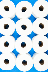 Background pattern of toilet paper rolls lay flat on the bright blue background. Coronavirus pandemic panic shopping concept. Vertical photo