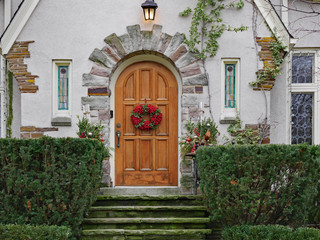 Fototapeta na wymiar House with wooden front door with wreath with red berries and moss covered flagstone steps