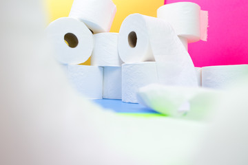 Pile of toilet paper rolls and one roll in front with camera wrapping effect on yellow blue pink color background hoarding amid panic buying for corona virus outbreak shortage.
