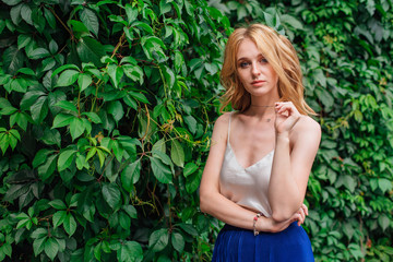 Portrait of a young beautiful woman, standing next to the wall of wild grape leaves.