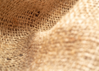 Fototapeta na wymiar Crumpled burlap fabric, close up view. Texture of brown sackcloth. Brown burlap textile, abstract background. Selective soft focus. Blurred background