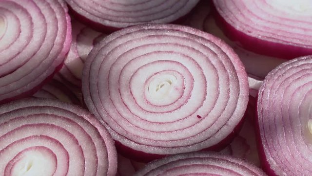 Sliced red onion rings rotating on white in 4K. Closeup top view of healthy food background with vegetable of rich vitamin.