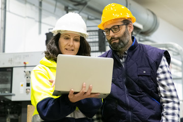Front view of two employees talking while standing with laptop. Confident technicians discussing working process. Manufacturing concept