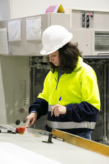 Serious professional milling machine operator standing at her workplace. Middle aged woman in uniform and helmet working at plant. Machinery or production concept