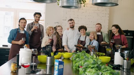 Portrait of happy men and women cooking school students smiling holding food and drinks looking at camera and wearing aprons. People and emotions concept.