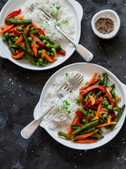 Green beans, sweet peppers, carrots, onions, green peas stir fry and rice on a dark background, top view. Fast diet vegetarian lunch