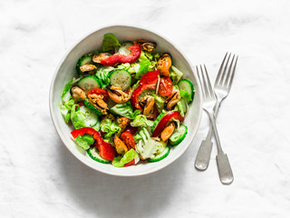 Salad with fresh vegetables and canned mussels on a light background, top view. Delicious healthy...
