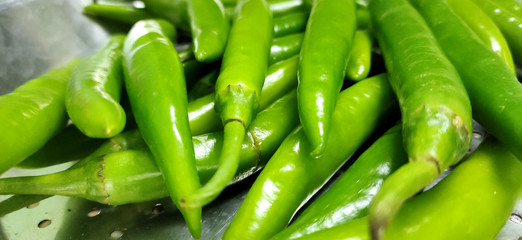 Full frame close up of a bunch of bright and shiny green chili peppers. Organic vegetables at the local food market.