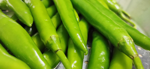 Full frame close up of a bunch of bright and shiny green chili peppers. Organic vegetables at the local food market.