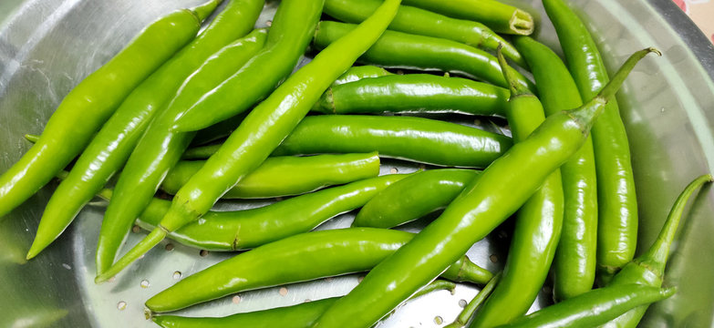 Full frame close up of a bunch of bright and shiny green chili peppers. Organic vegetables at the local food market.