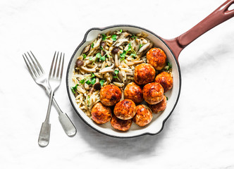 Orzo mushrooms pasta with teriyaki sauce chicken roasted meatballs in a pan on a light background, top view