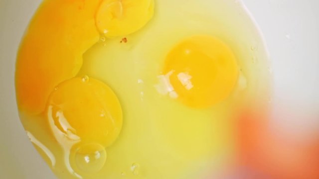 Macro top shot of two raw yellow egg yolks in white dish, one egg yolk added in