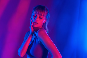 Cool stylish sexy young adult beautiful woman stand in fashion pose at purple studio background. Attractive sensual blond hair 20s girl model dance in neon party trendy 90s light concept.
